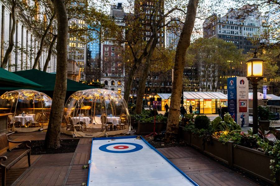 An iceless curling lane and heated dining dome sit on the Bryant Park Café deck during winter, part of the Winter Village Curling Café.