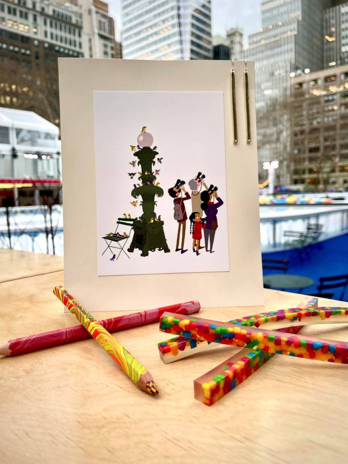 Coloful pencils and crazy erasers lie in front of a Bryant Park print with the rink in the background in New York City.