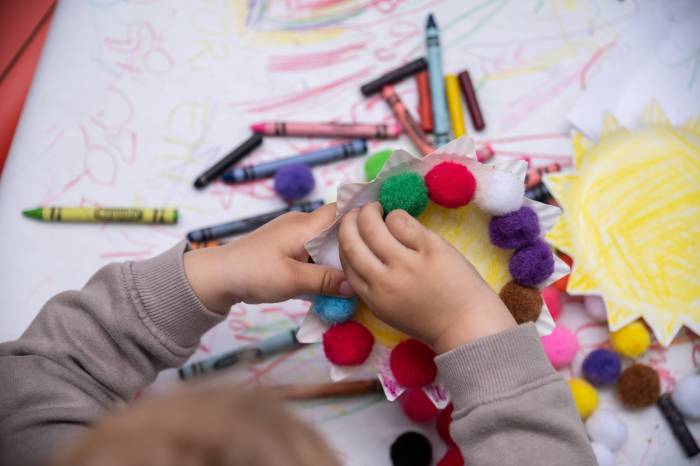 Child placing colored pom poms onto a paper plate