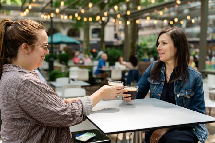 Two women toast with espresso martinis at Bryant Park's outdoor bar and cafe, L'OR Porch.