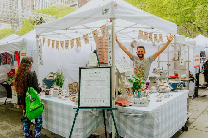 A vendor throws his arms up in the air in joy at his outdoor booth at Urbanspace’s Spring Makers Market, located in Bryant Park NYC.