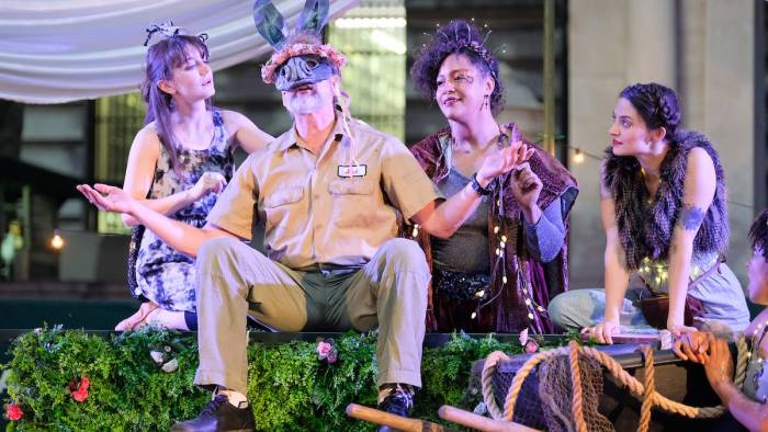 Three actors from the Drilling Company sit on an outdoor stage in Bryant Park New York City, performing A Midsummer Night's Dream.