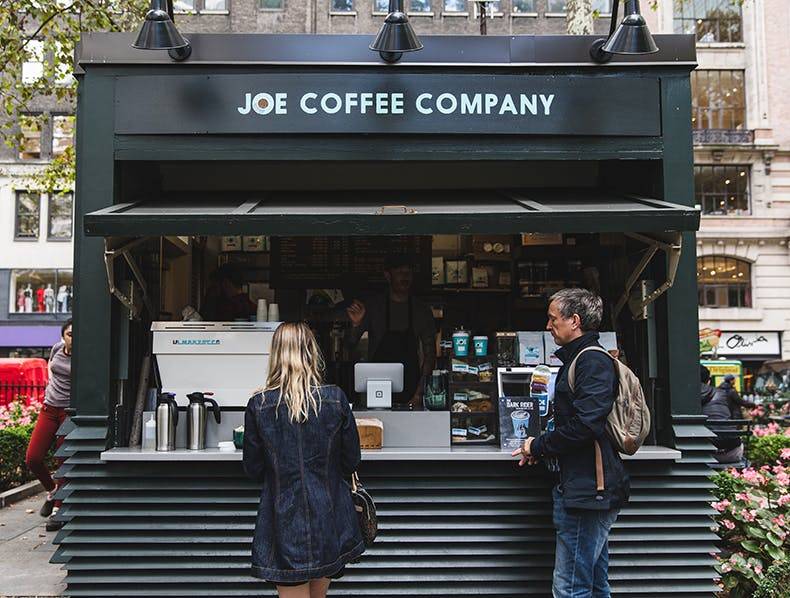 People standing outside at the Joe Coffee kiosk ordering coffee at Bryant Park NYC.